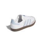 White sneaker with light blue stripes and brown gum sole, viewed from the rear-left side in low angle light