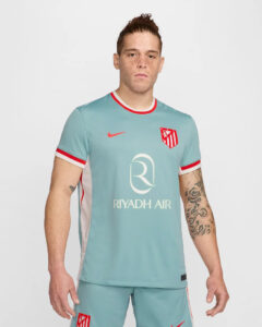 Man wearing light blue football jersey with Riyadh Air sponsor and Atlético Madrid crest, posing against a white background.
