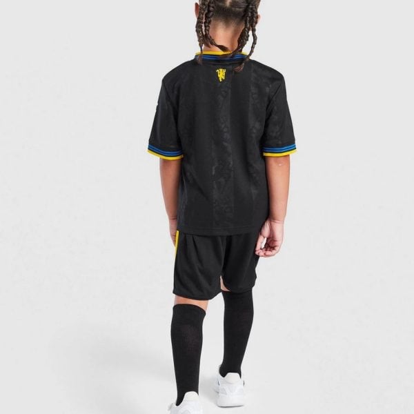 Child wearing a black soccer jersey and shorts, viewed from the back, with yellow and blue trim and long black socks.