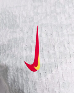 Red Nike swoosh logo with a yellow inner accent on a textured white fabric background (close-up)