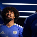 Soccer player with curly hair and goatee in a blue Leicester City jersey in a dim tunnel environment.