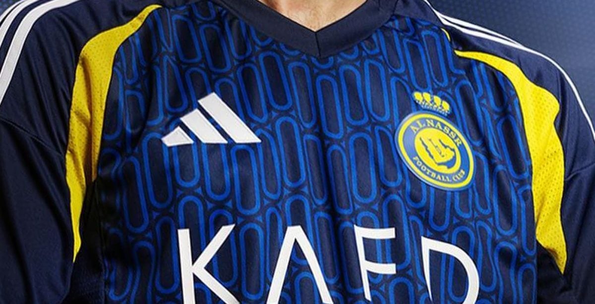 Close-up of a blue Adidas sports jersey with yellow shoulders, a team crest on the left chest, and large 'KAED' text across the front.