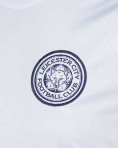 White shirt with a circular Leicester City Football Club crest featuring a fox head at the center on the chest area.