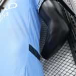 Close-up of a light-blue sports jersey and a black forearm guard resting against a metal fence.