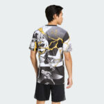 Back view of a man wearing a bold graphic T-shirt with black, white, and yellow comic-style panels, standing against a light backdrop.