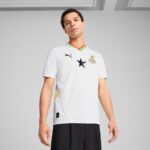 Young man in a white soccer jersey with a black star, Ghana Football Association crest, and Puma logo, standing against a gray background.