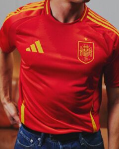 Person wearing a red Spain national team jersey with yellow shoulder stripes and crest, standing with hands on hips.