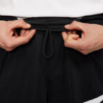 Person tightening the drawstring on black waistband shorts/pants.
