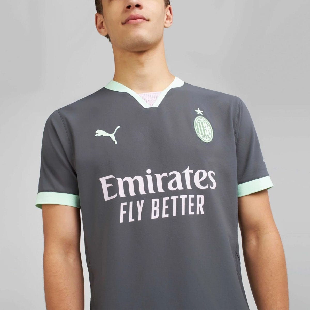 Man wearing a dark gray soccer jersey with light green trim, Puma logo on left chest and AC Milan crest on right, 'Emirates Fly Better' across the front