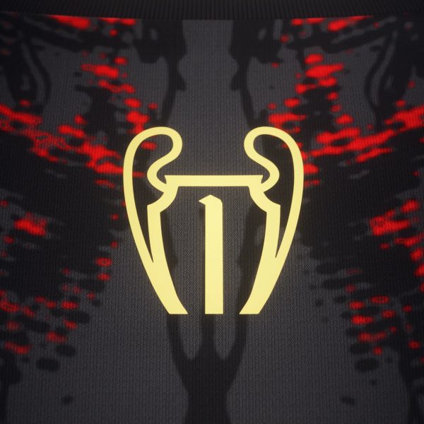 Close-up of dark fabric with a gold trophy-like outline and red speckled accents, and the text 'COMMA FOOTBALL' at the top.
