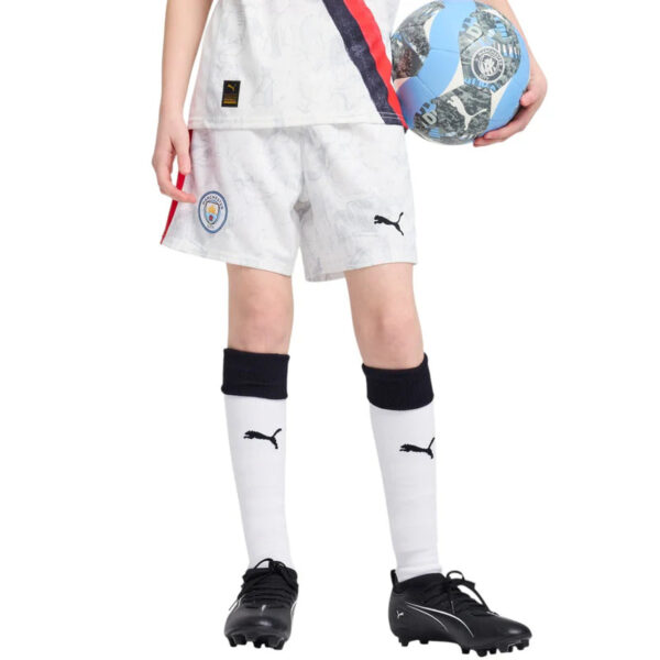 Young child in a white soccer uniform with team shorts, white socks, and black cleats, holding a blue and white soccer ball beside them.
