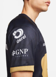 Side profile of a person wearing a navy sports jersey with white sponsor logos (Berel, GNP Seguros) and tan cuffed sleeves