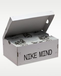Open white Nike Mind shoebox with lid raised, showing inner packaging and repeating 'NIKE MIND' text across an illustrated pattern.