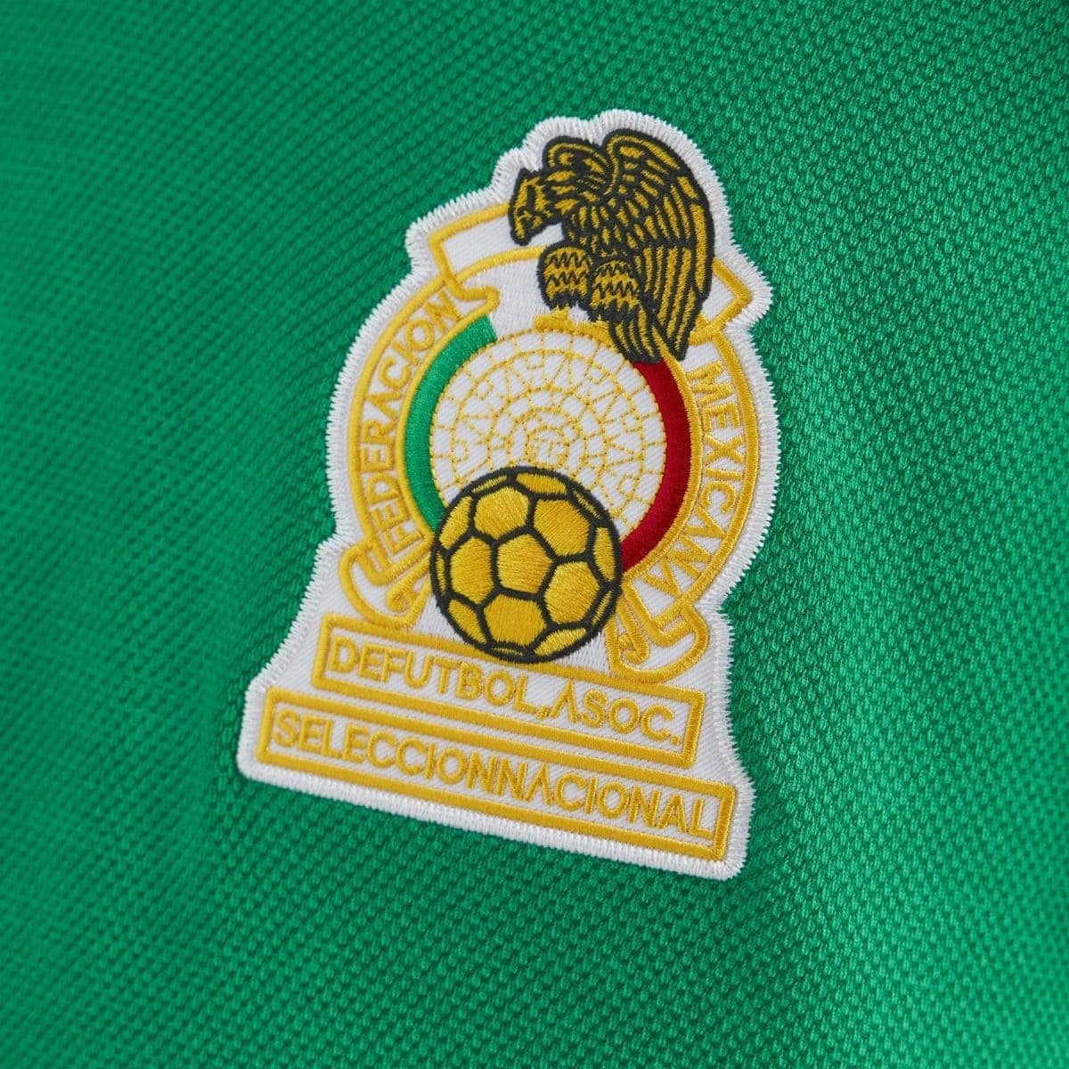 Close-up of an embroidered Mexican Football Federation crest on a green jersey fabric.