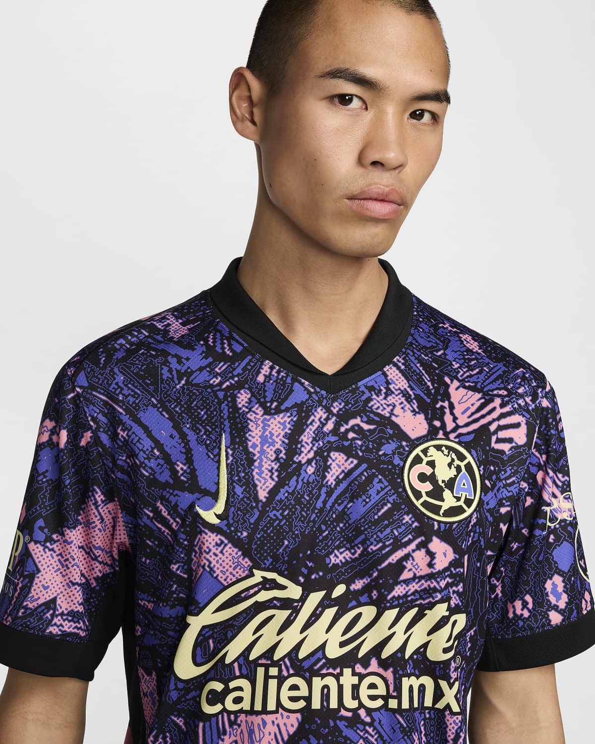 Man wearing a purple-pink camouflage-patterned sports jersey with 'caliente.mx' across the chest and a circular team crest on the upper left; close-up of upper body and face against a light background.