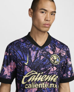 Man wearing a purple-pink camouflage-patterned sports jersey with 'caliente.mx' across the chest and a circular team crest on the upper left; close-up of upper body and face against a light background.