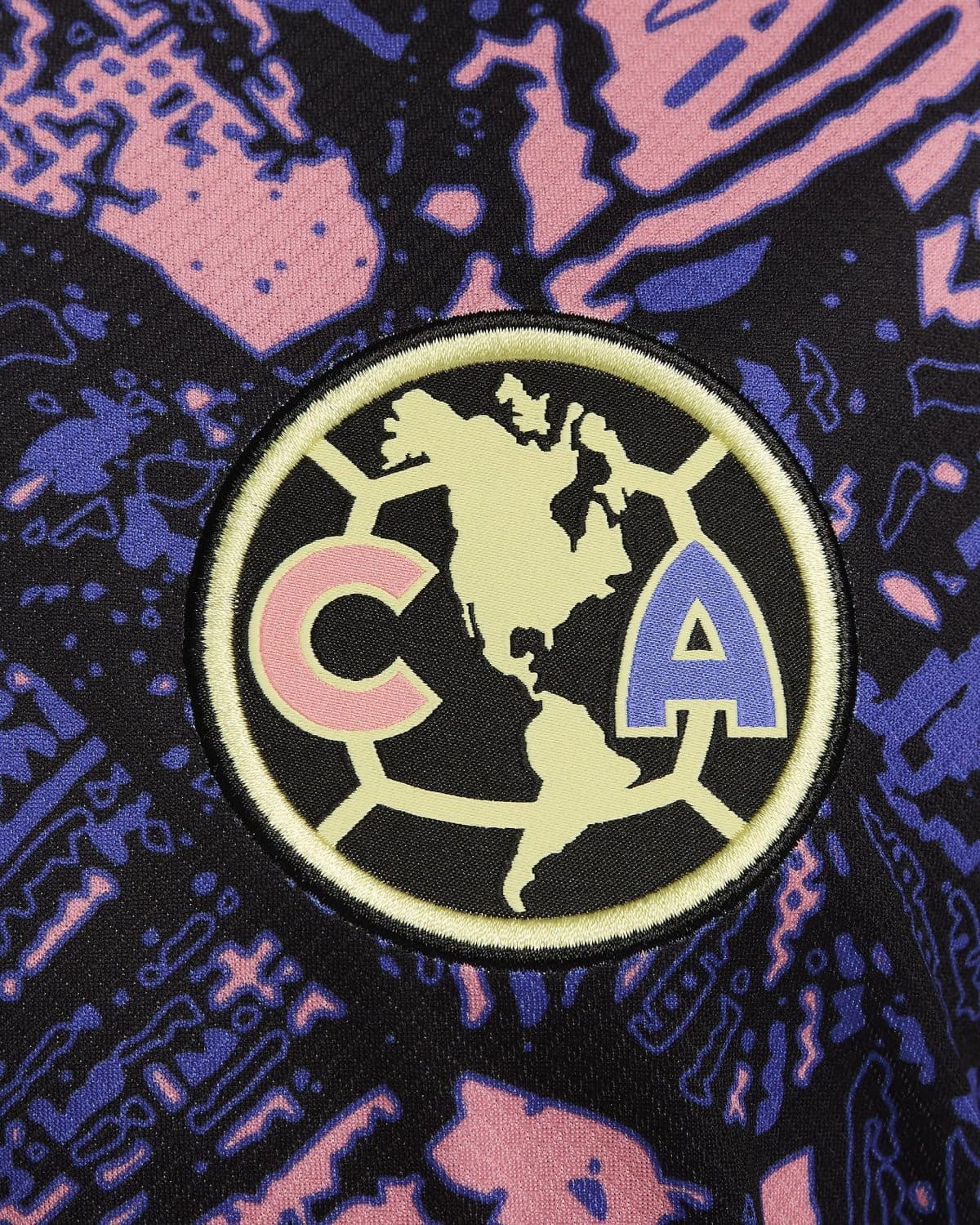 Close-up of a circular embroidered patch showing a beige world map and the letters CAP on dark fabric with pink and blue abstract patterns.