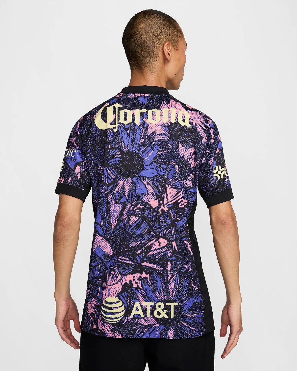 Back view of a person wearing a bold, purple-pink-blue abstract jersey with large yellow 'Corona' lettering across the upper back and an AT&T logo toward the lower back.