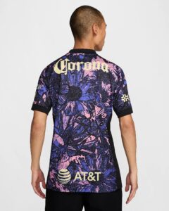 Back view of a person wearing a bold, purple-pink-blue abstract jersey with large yellow 'Corona' lettering across the upper back and an AT&T logo toward the lower back.