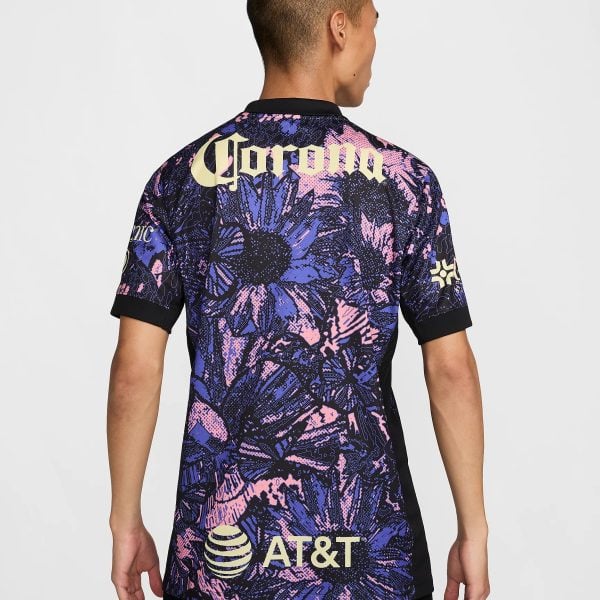 Back view of a person wearing a bold, purple-pink-blue abstract jersey with large yellow 'Corona' lettering across the upper back and an AT&T logo toward the lower back.