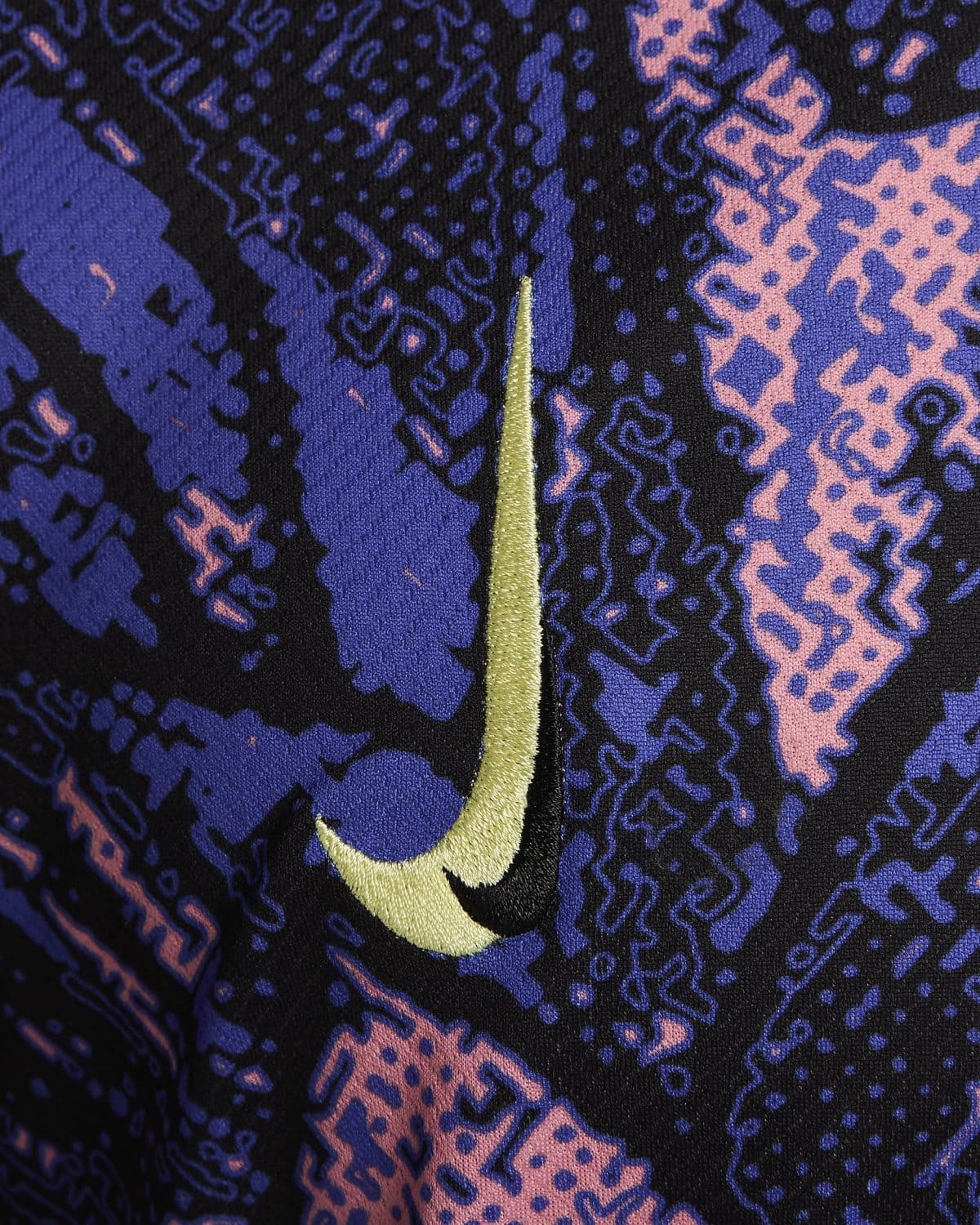 Close-up of a gold Nike swoosh embroidered on dark blue and pink patterned fabric.