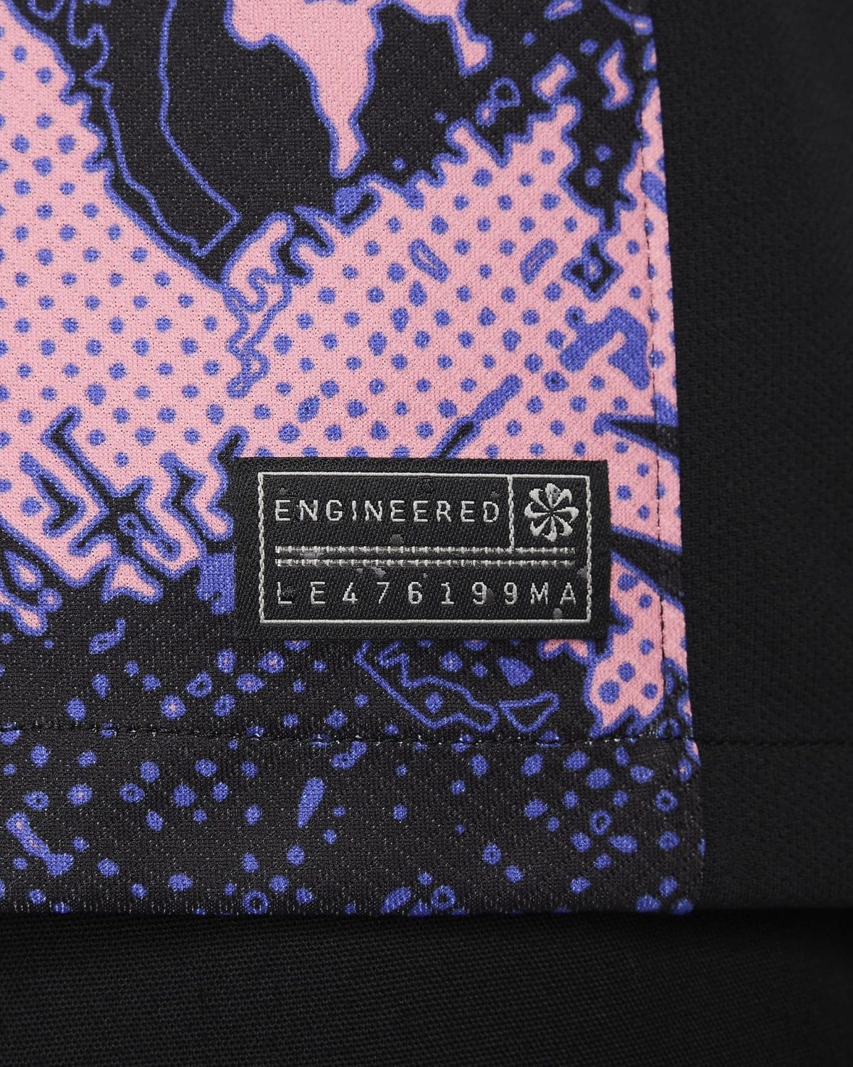 Close-up of pink fabric with blue dots and a black woven tag reading ENGINEERED with numbers below it.