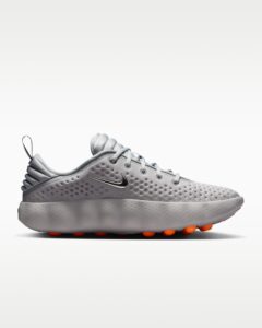Close-up of a gray athletic sneaker showing the dotted upper, laces, and orange-tipped studs on the sole with a metallic swoosh.