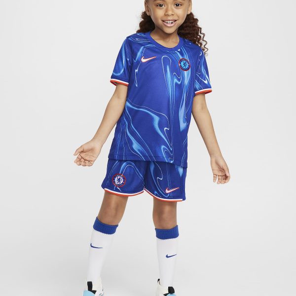 Young girl in a blue Chelsea FC soccer kit with white socks, smiling, facing forward against a light background.