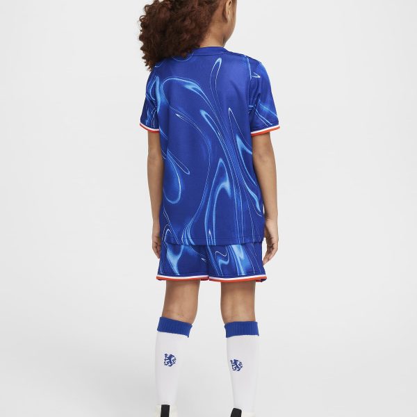 Back view of a young player in a blue abstract-pattern soccer jersey and shorts, white knee-high socks, and white cleats, standing against a white background with curly hair tied back.