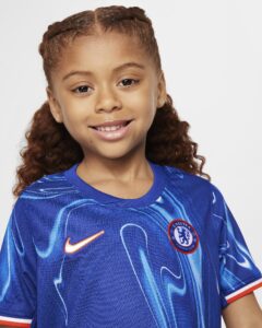 Young girl smiling in a blue Chelsea FC football jersey with a Nike swoosh and crest showing on the chest.