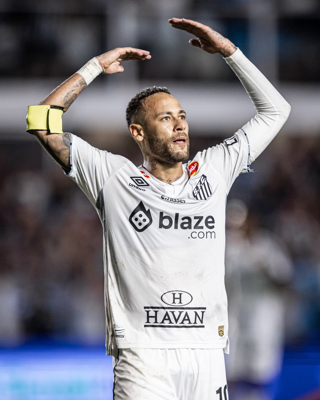 CFeeLe35jZu7qDq | UAE SPORT STORE Santos FC player in a white kit raises arms in celebration, forming a heart shape above his head on the pitch.