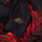 Close-up of black fabric with red lining and a small gold crest near a seam.