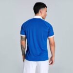 Man seen from behind wearing a bright blue polo shirt with white collar and sleeve trim; white shorts visible at the bottom.