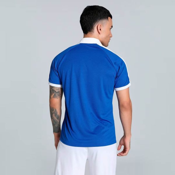 Man seen from behind wearing a bright blue polo shirt with white collar and sleeve trim; white shorts visible at the bottom.