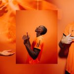 CSV0V9isaqJp2Lr | UAE SPORT STORE Portrait of a man in an orange jersey, looking up with hands raised, against an orange backdrop.