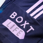 Close-up of a dark navy athletic jacket with light pink text reading 'BOXET LIFE' and pale pink stripes.