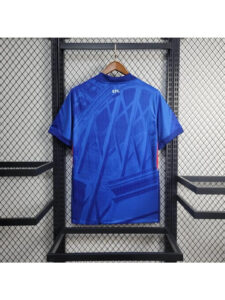 Camiseta-Chelsea-FC-1_-Equipacion-2526camisetafutboles_1-1080x1440-1 | UAE SPORT STORE Blue athletic jersey hanging on a wooden hanger, back view with abstract diagonal patterns and a small CFC logo near the collar.