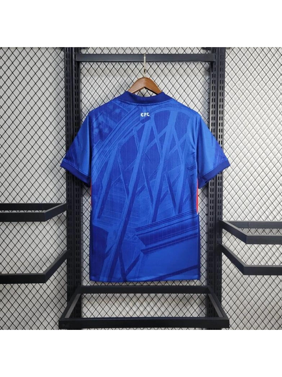 Camiseta-Chelsea-FC-1_-Equipacion-2526camisetafutboles_1-1080x1440-1 | UAE SPORT STORE Blue athletic jersey hanging on a wooden hanger, back view with abstract diagonal patterns and a small CFC logo near the collar.