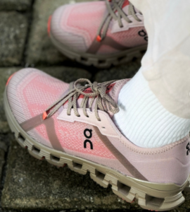 Capture_2b5ad184-93a6-4230-a043-58d811a67a7b | UAE SPORT STORE Pink On running shoes with gray laces and white socks standing on a stone pavement surface.