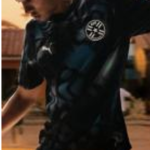 Male athlete wearing a black athletic shirt with a circular white logo on the chest, in motion outdoors at sunset.