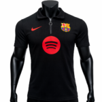 Black polo shirt with a zip collar, displaying a red Nike swoosh on the left chest, a Barcelona crest on the right chest, and a large red Spotify logo centered on the front.