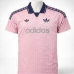 Pink Adidas jersey with navy collar, three navy stripes on shoulders, trefoil logos, and large 'adidas' branding across the chest.