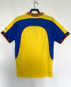 Back view of a yellow and blue sports jersey hanging on a hanger, with red piping along the seams and a striped collar.