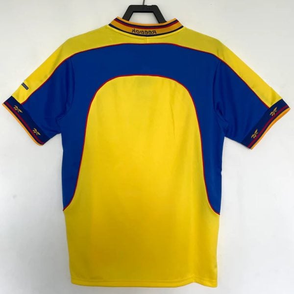 Back view of a yellow and blue sports jersey hanging on a hanger, with red piping along the seams and a striped collar.