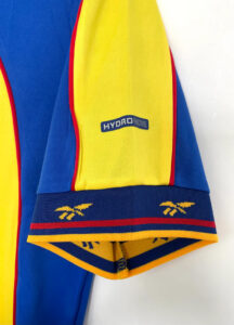 Close-up of a blue-and-yellow sports jersey sleeve with red piping and a Hydro Move logo on the yellow panel.