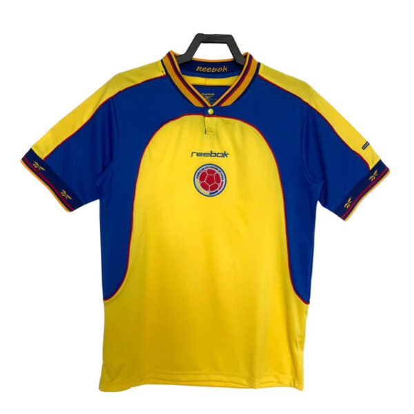 Colombia national football jersey in yellow with blue side panels, featuring Reebok logo and the team crest at the chest on a hanger.