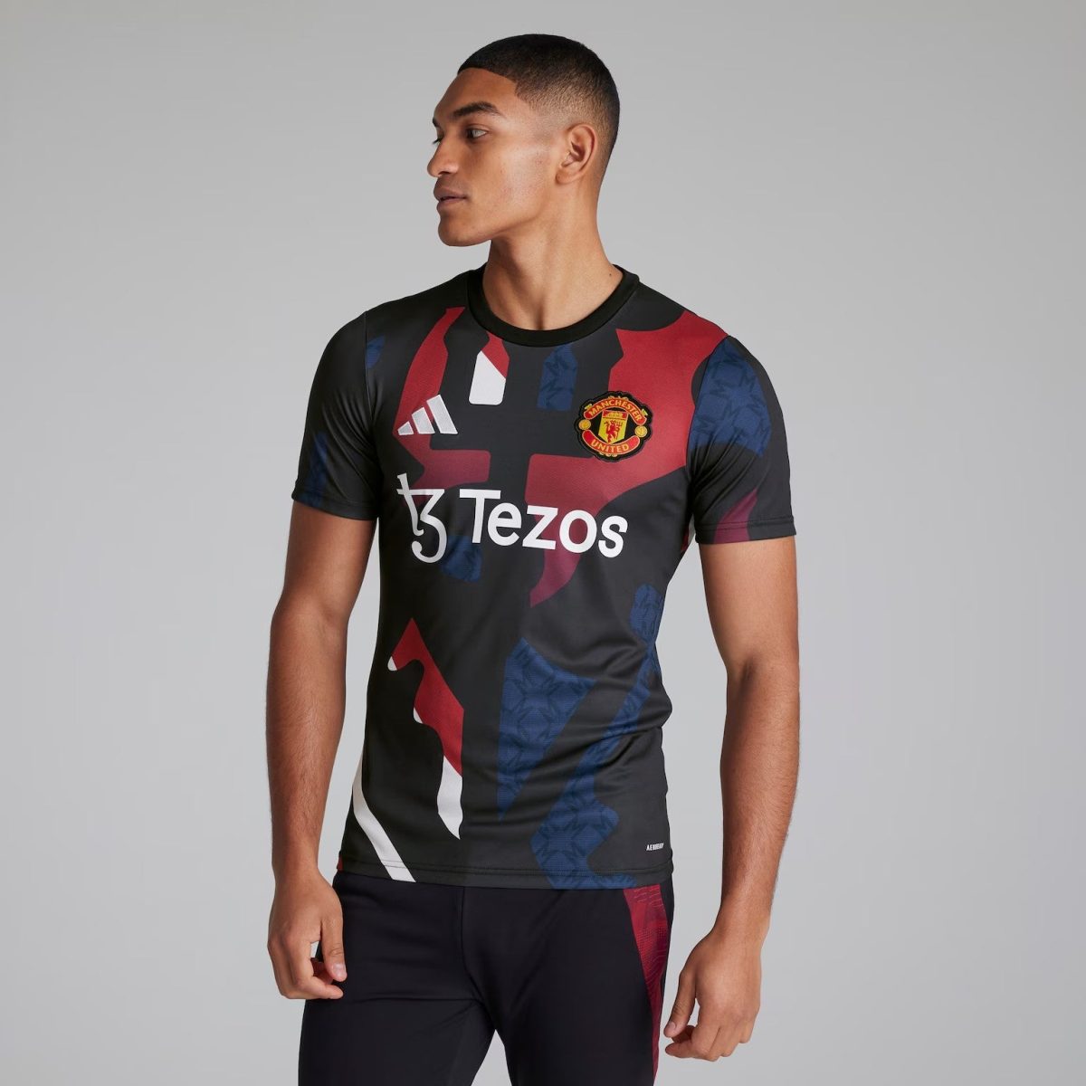 Man wearing a black Manchester United jersey with red and blue geometric pattern and Tezos sponsor, looking to the left.