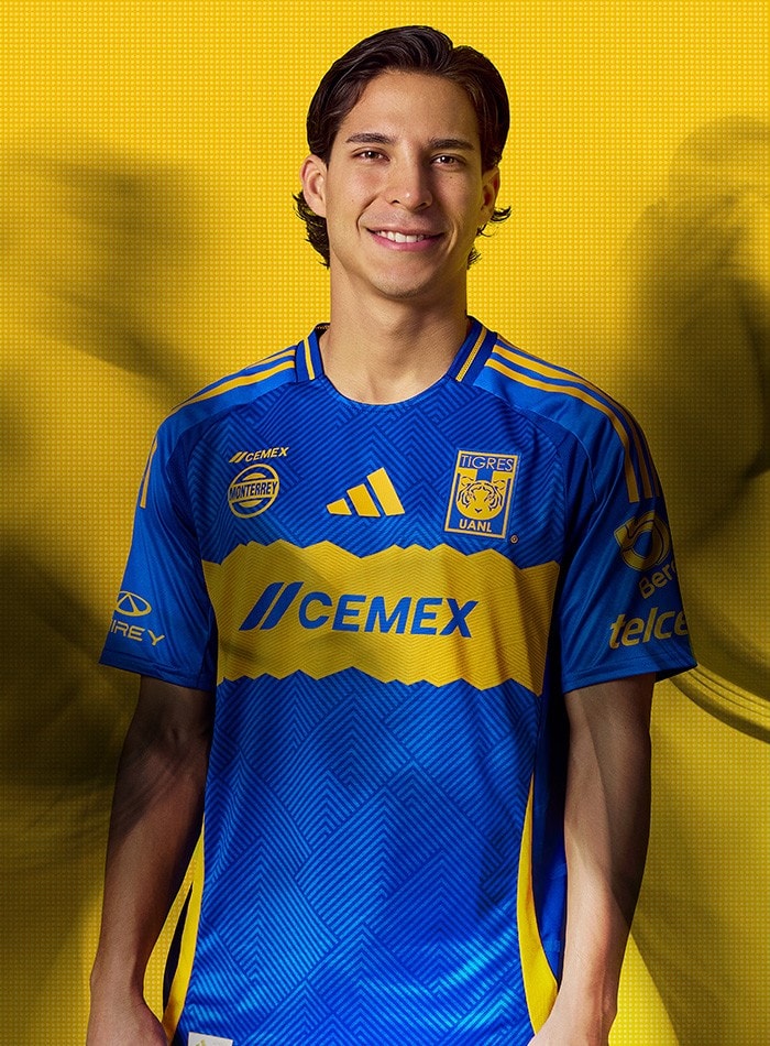 CvYdK4SD4hVplsH | UAE SPORT STORE Young man wearing a blue and yellow Tigres UANL soccer jersey with sponsor logos, standing against a solid yellow background.