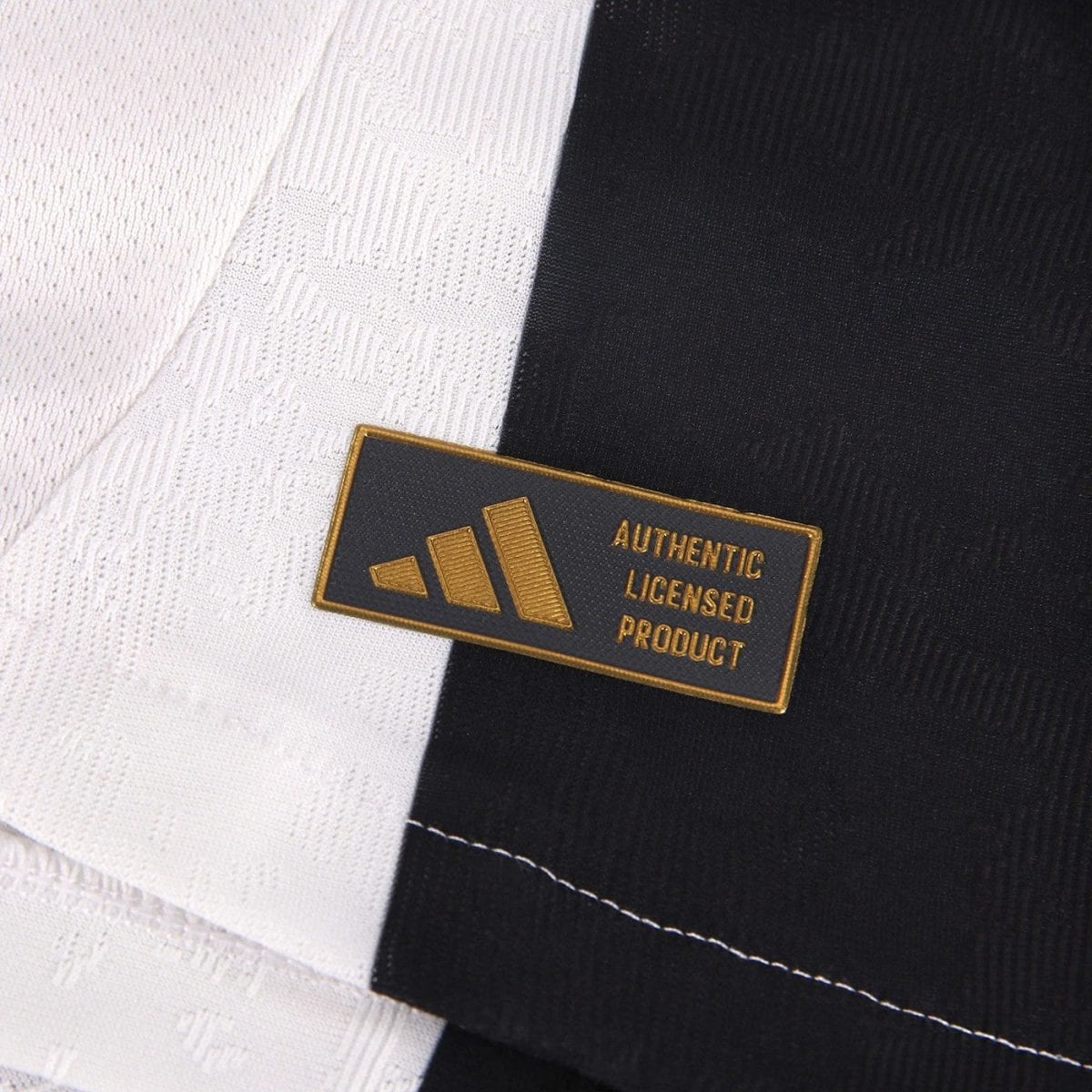 Gold embroidered patch reading 'AUTHENTIC LICENSED PRODUCT' on black fabric, with white textile background nearby.