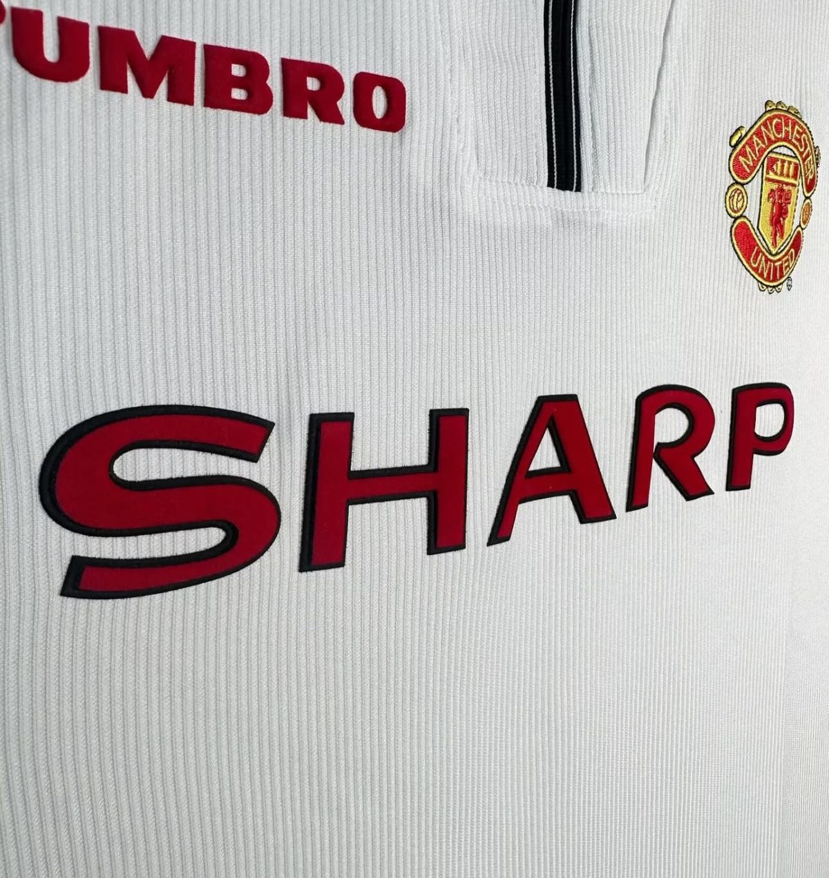 Close-up of a Manchester United white jersey with red SHARP sponsor lettering and crest.